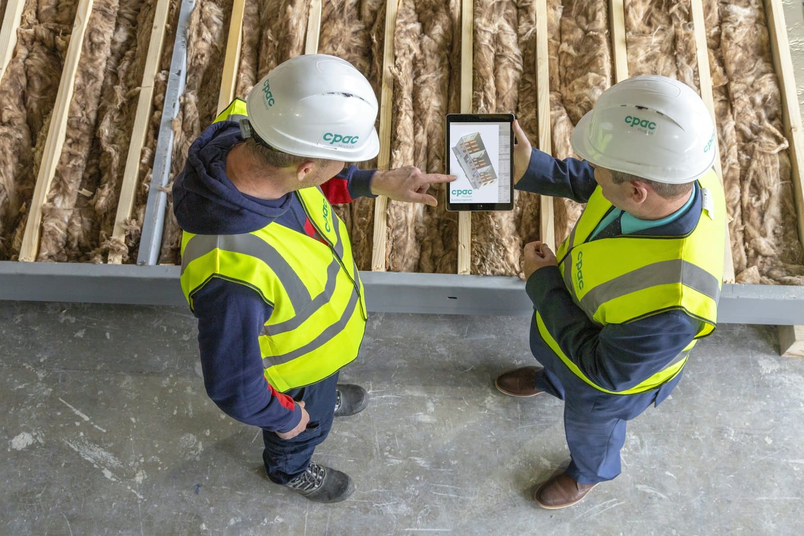 Deux artisans consultent un plan sur une tablette dans un bâtiment en construction